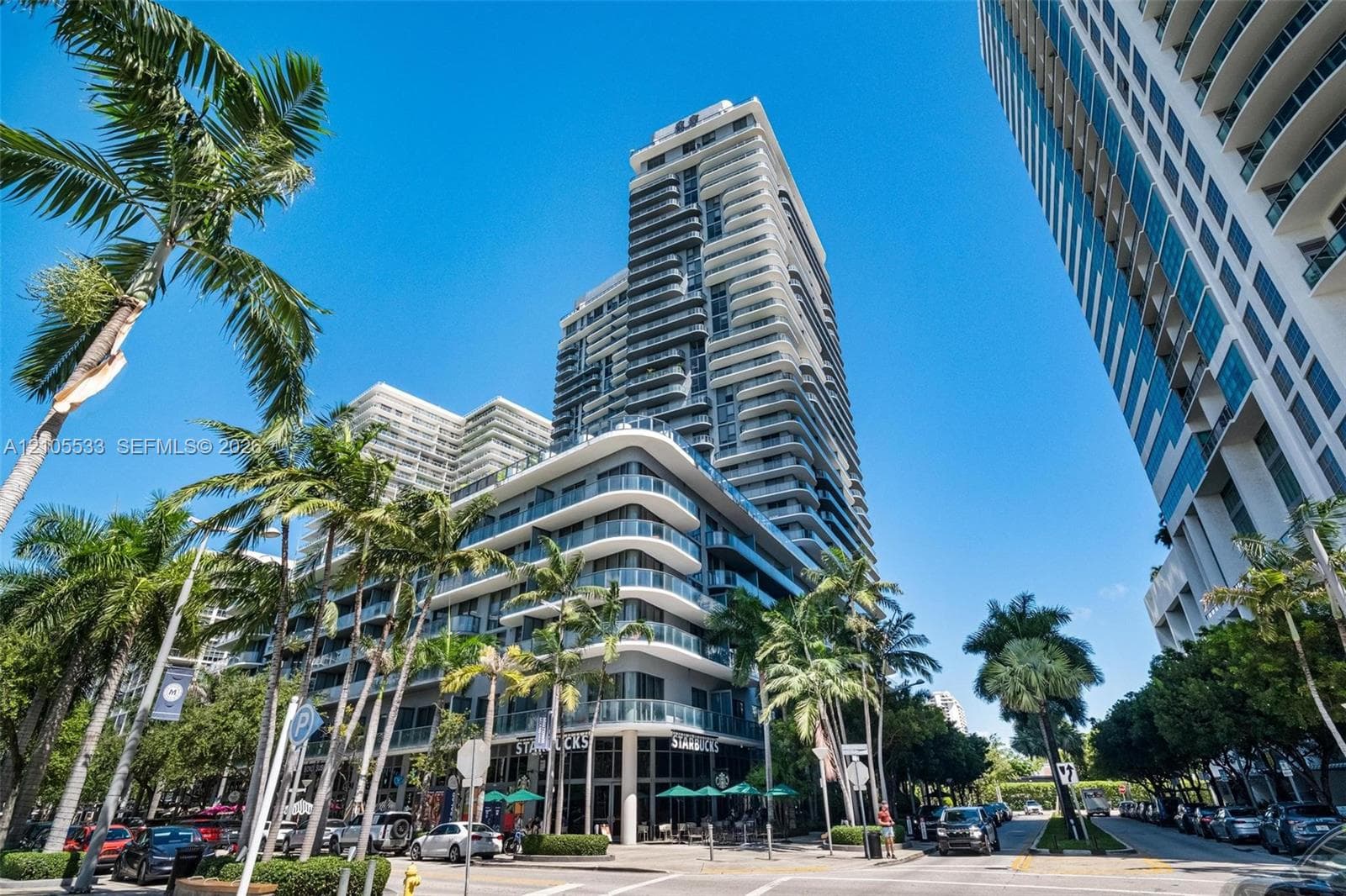 High-rise exterior featuring concrete structural design, tiered balconies with glass railings, and expansive floor-to-ceiling windows