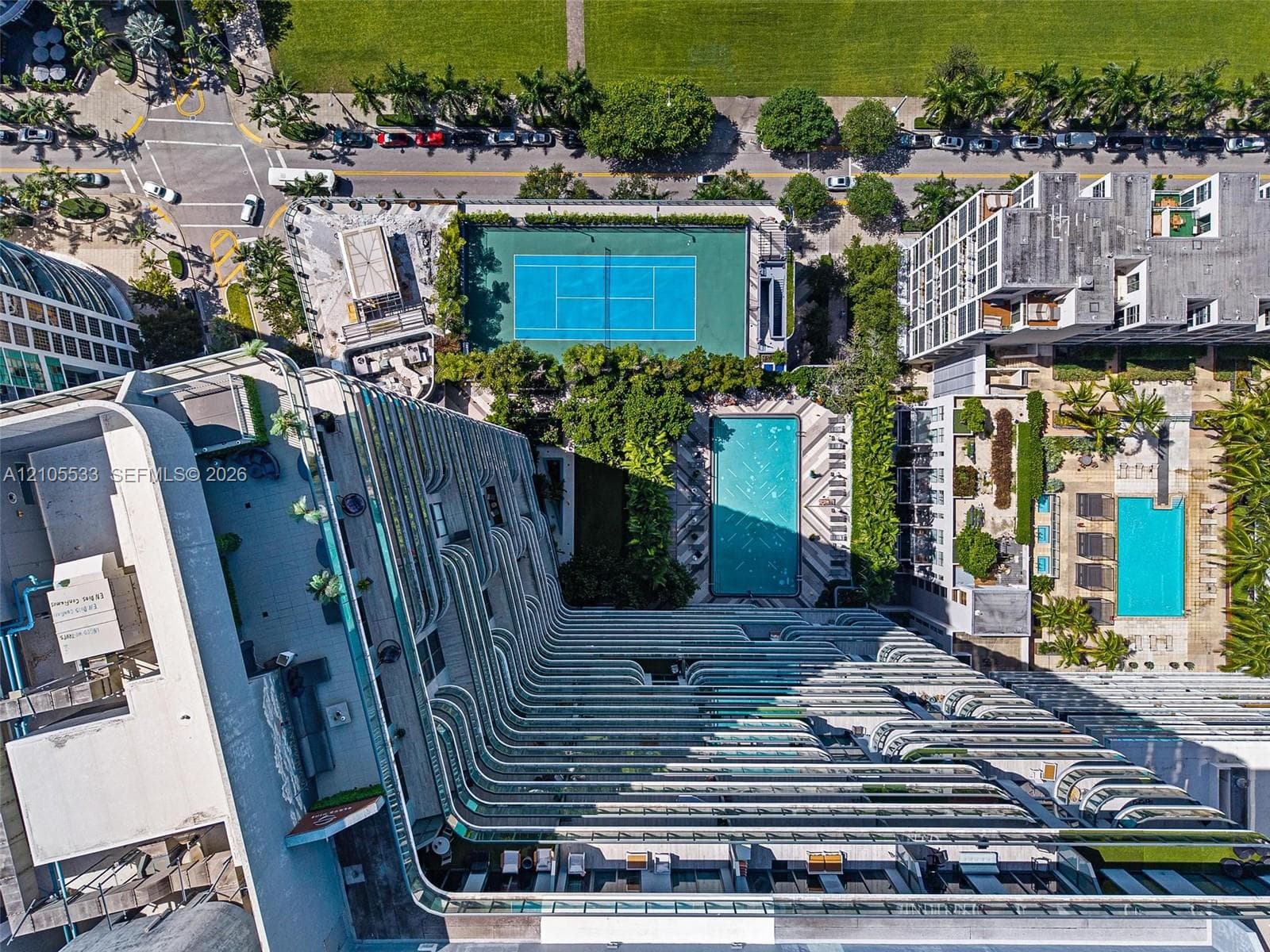 High-rise building featuring curvilinear wrap-around balconies, a ground-level swimming pool, and an outdoor tennis court