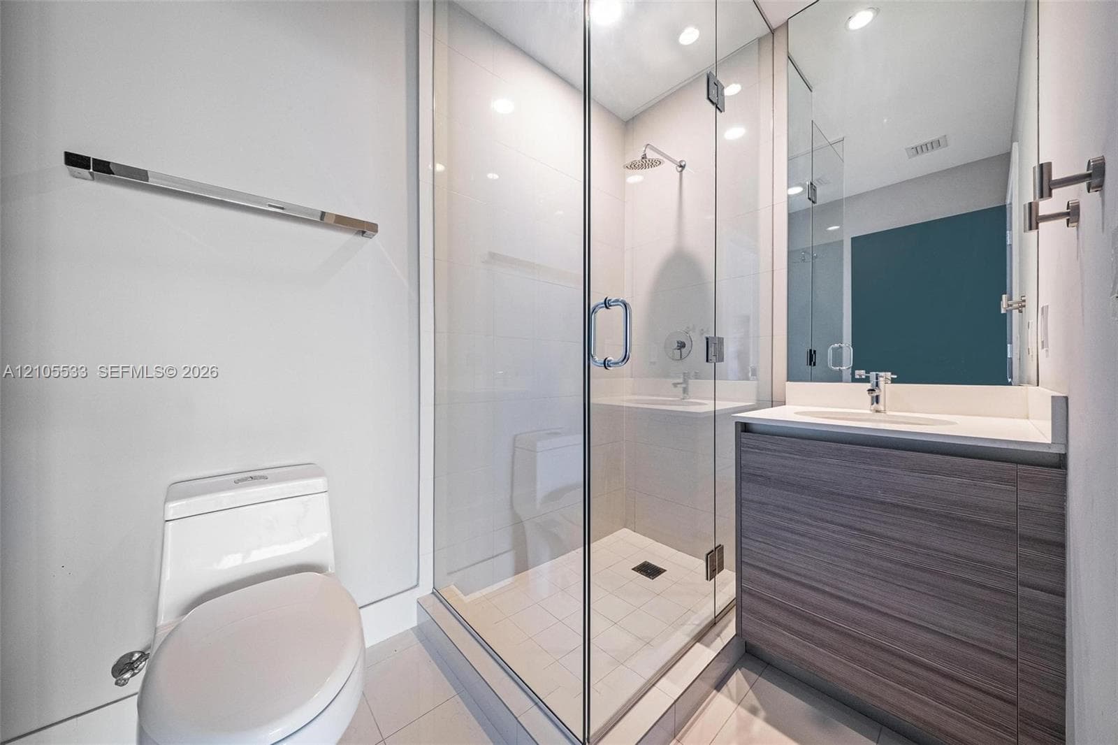 Bathroom featuring a glass-enclosed shower with a rainfall showerhead, a wood-finish vanity with a solid-surface countertop, an integrated sink, and chrome fixtures