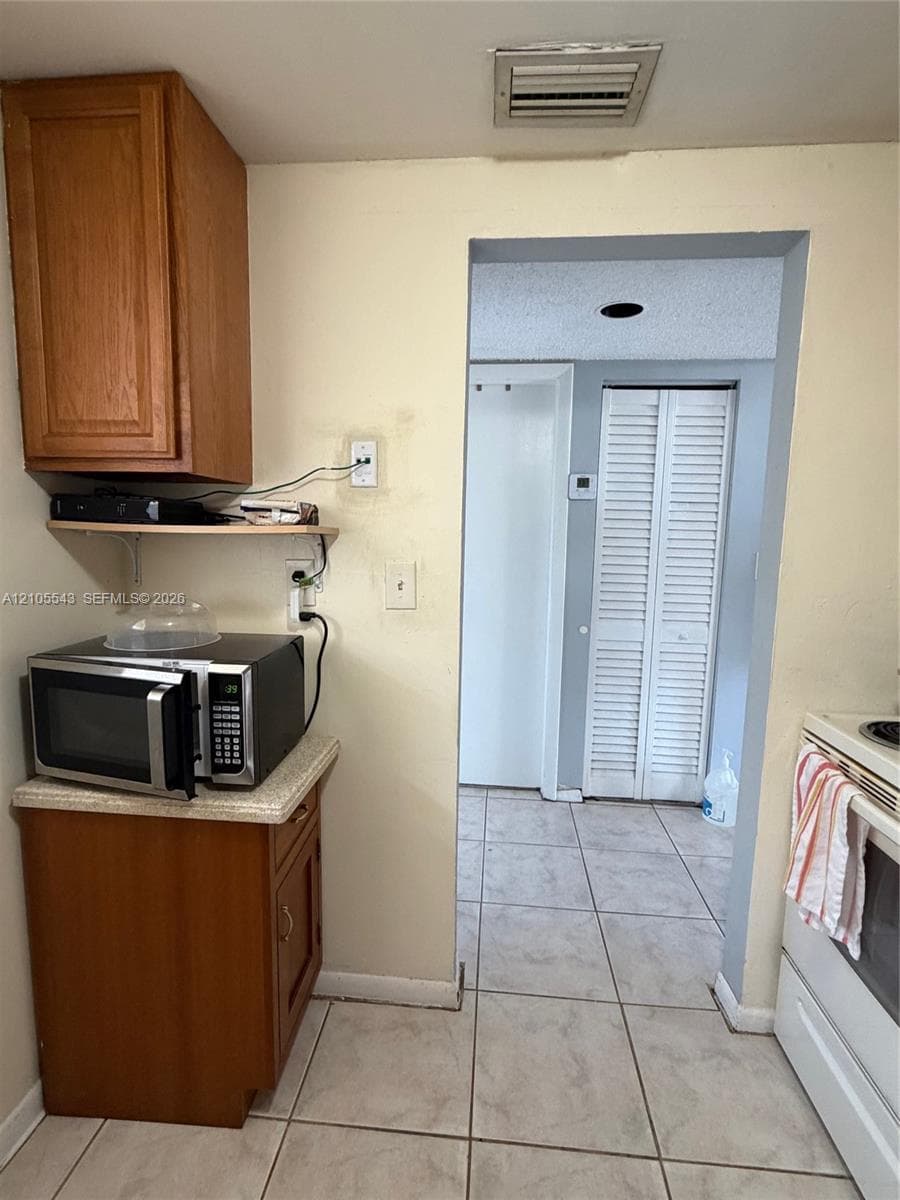 Kitchen featuring wood cabinetry, laminate countertops, ceramic tile flooring, and closet doors with louvered panels