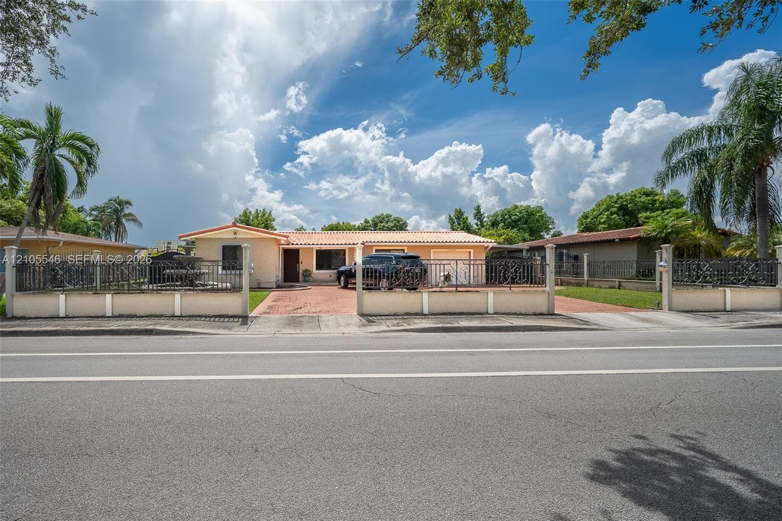 Single-story residence featuring a Spanish tile roof, paver driveway, and an enclosed perimeter with decorative metal fencing
