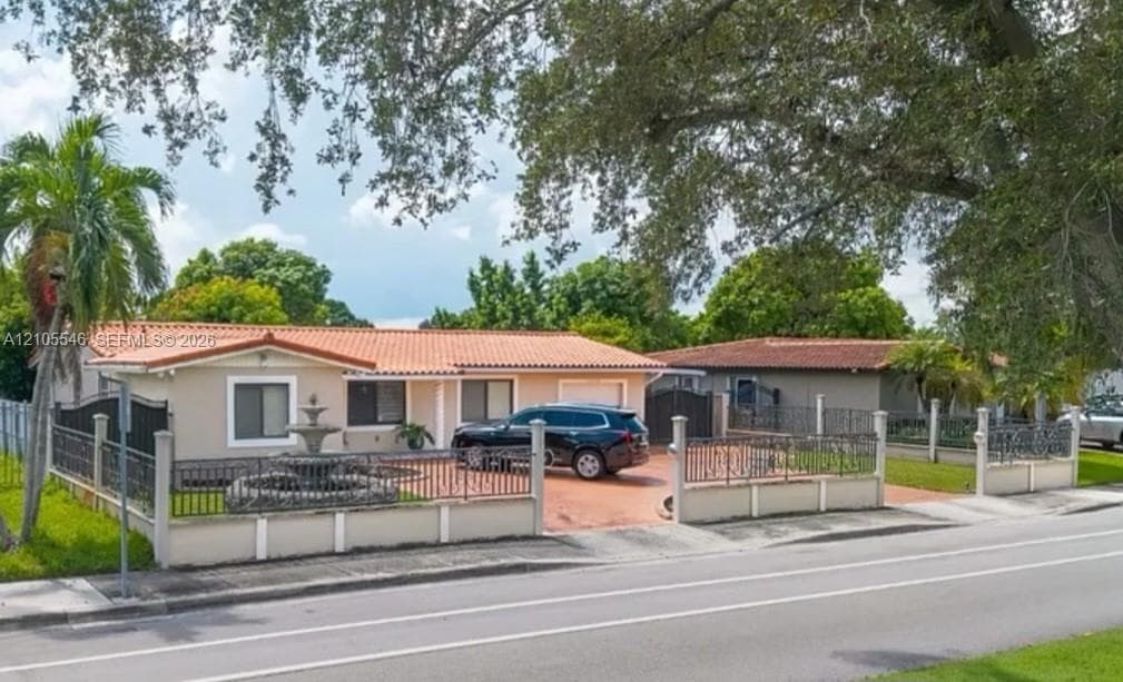 Exterior facade featuring a Spanish-style tile roof, decorative concrete fountain, paved driveway, and iron perimeter fencing with masonry pillars