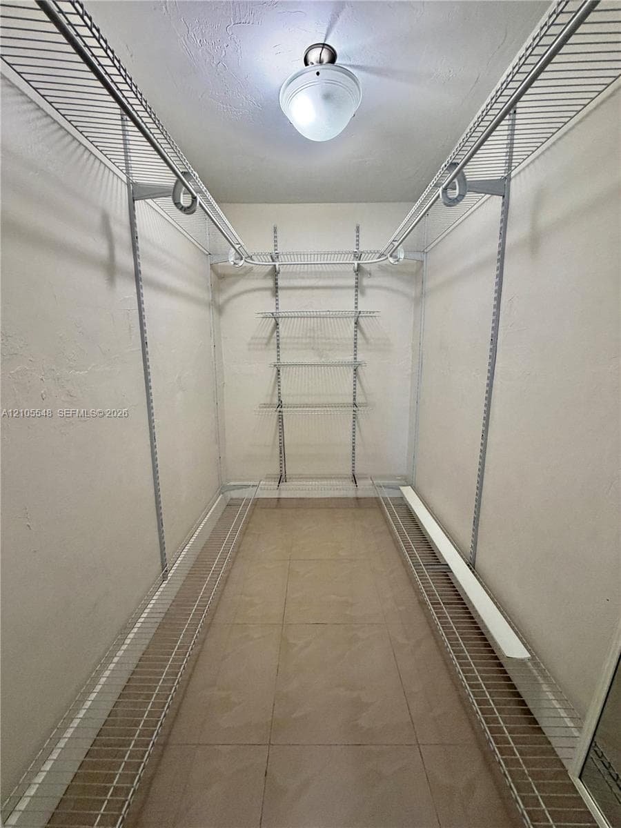 Walk-in closet in Primary bedroom, featuring tile flooring, white wire shelving, dual hanging rods, and a ceiling-mounted light fixture