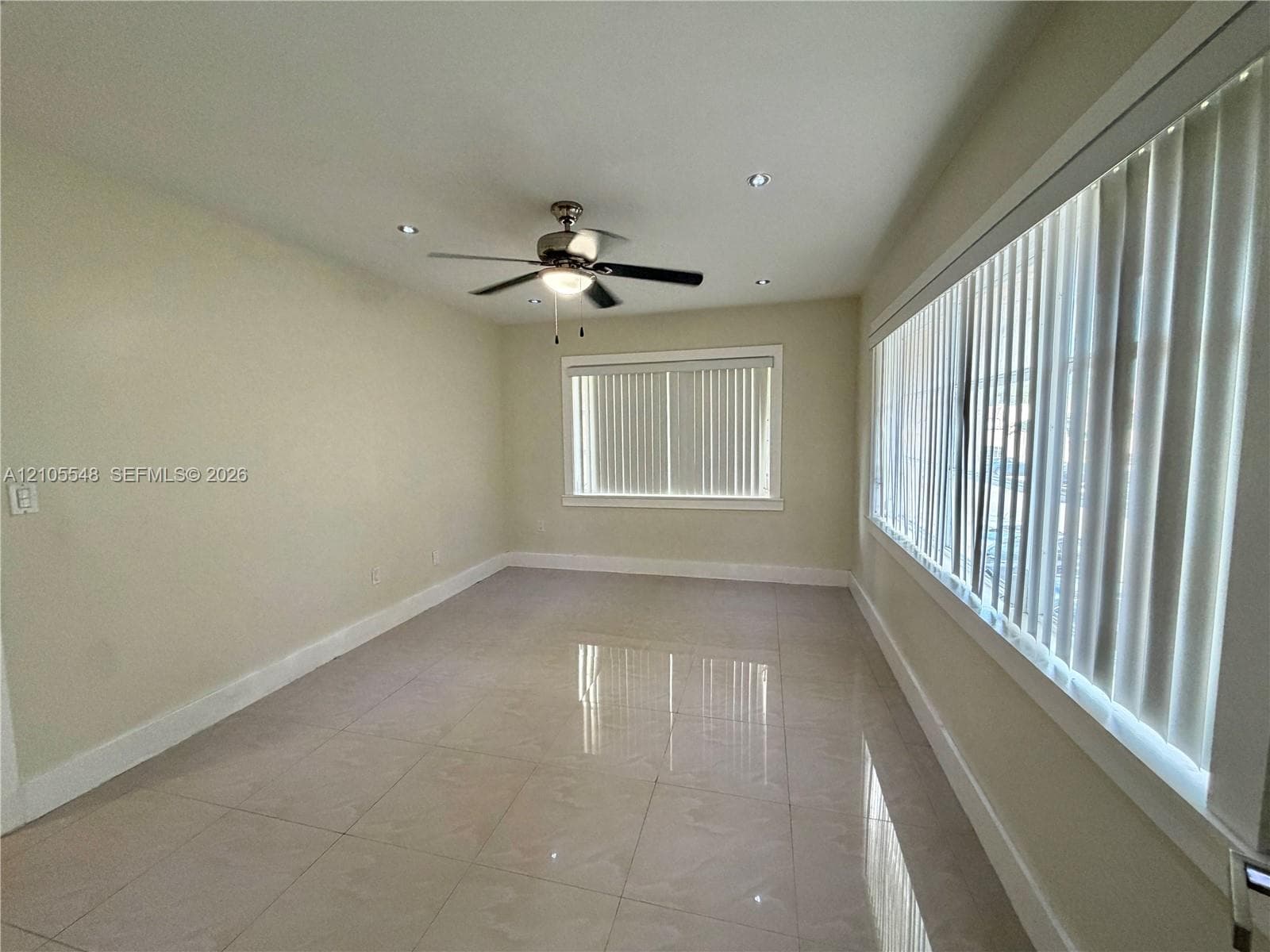 Neutral-toned interior featuring large-format porcelain tile flooring, recessed ceiling lighting, a central ceiling fan, and extensive windows dressed with vertical blinds