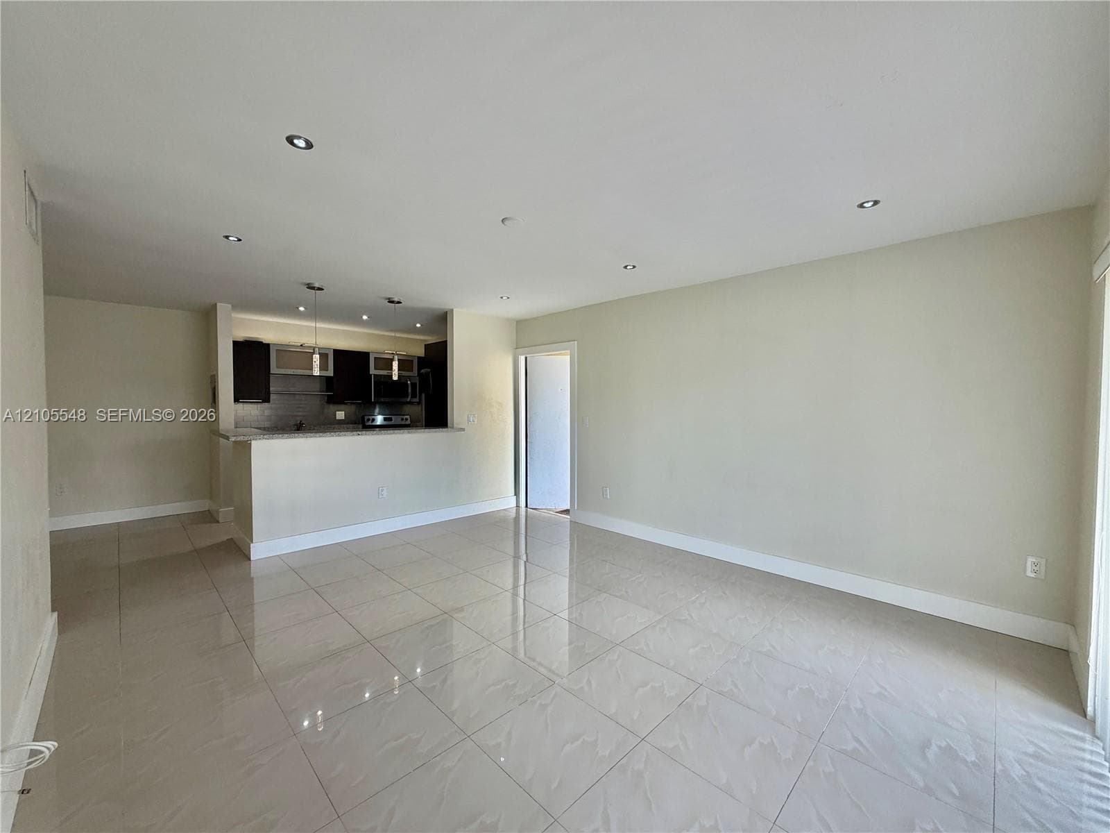 Open-concept interior featuring large-format porcelain tile flooring, recessed lighting, and kitchen with modern cabinetry, countertop peninsula, and pendant lighting