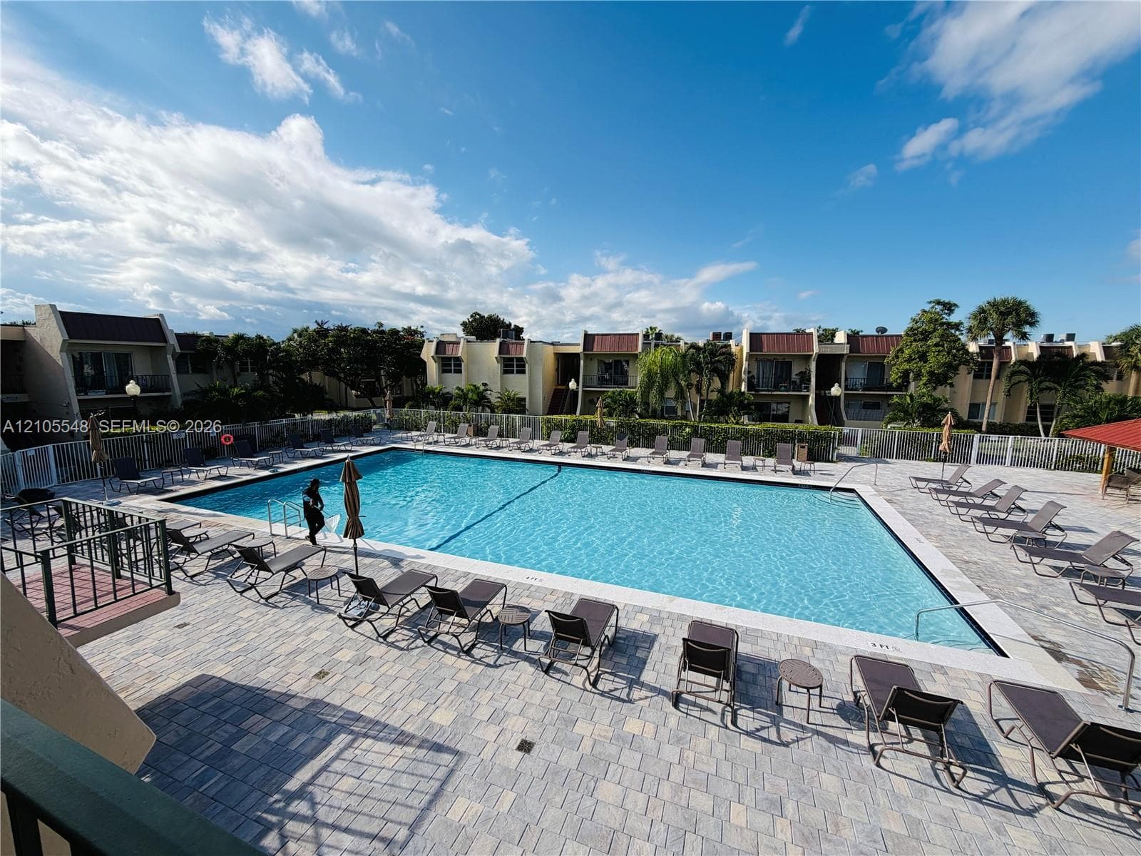 In-ground swimming pool with a stone paver deck, perimeter fencing, and a shaded pavilion