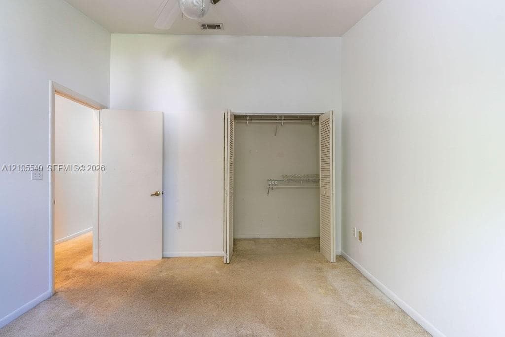 Neutral wall finishes, carpeted flooring, a ceiling-mounted fan, an open closet with bi-fold doors, and wire shelving