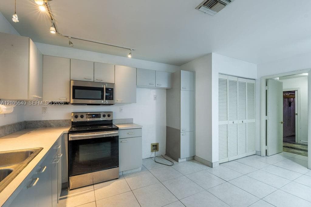Kitchen featuring white cabinetry, stainless steel appliances, track lighting, a double basin sink, and tile flooring