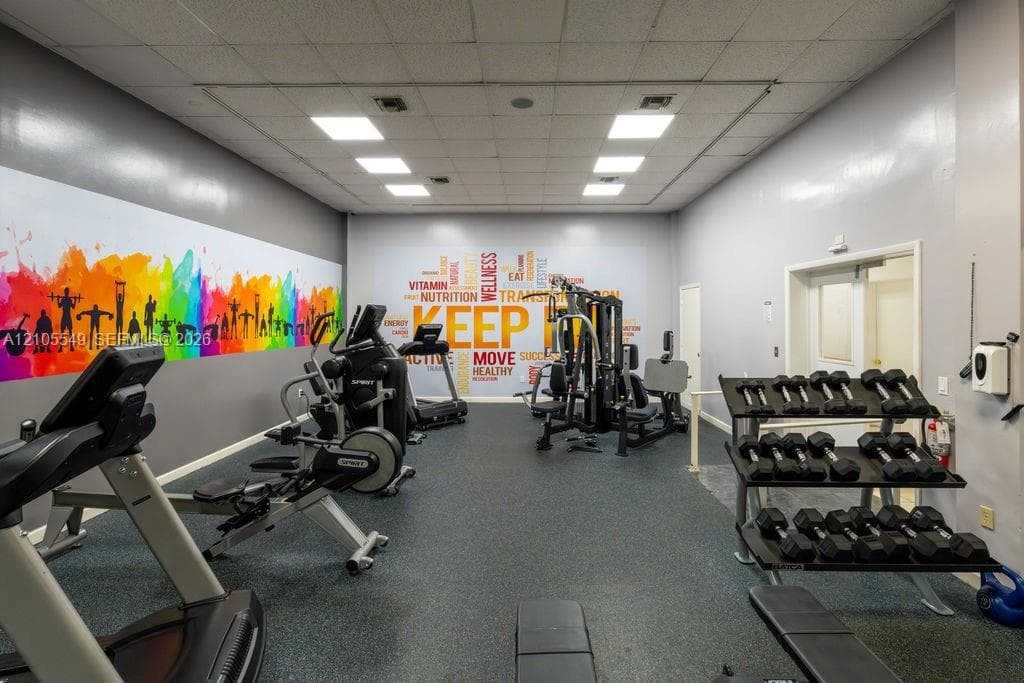 Fitness center featuring rubber flooring, drop ceiling with integrated lighting, and painted walls