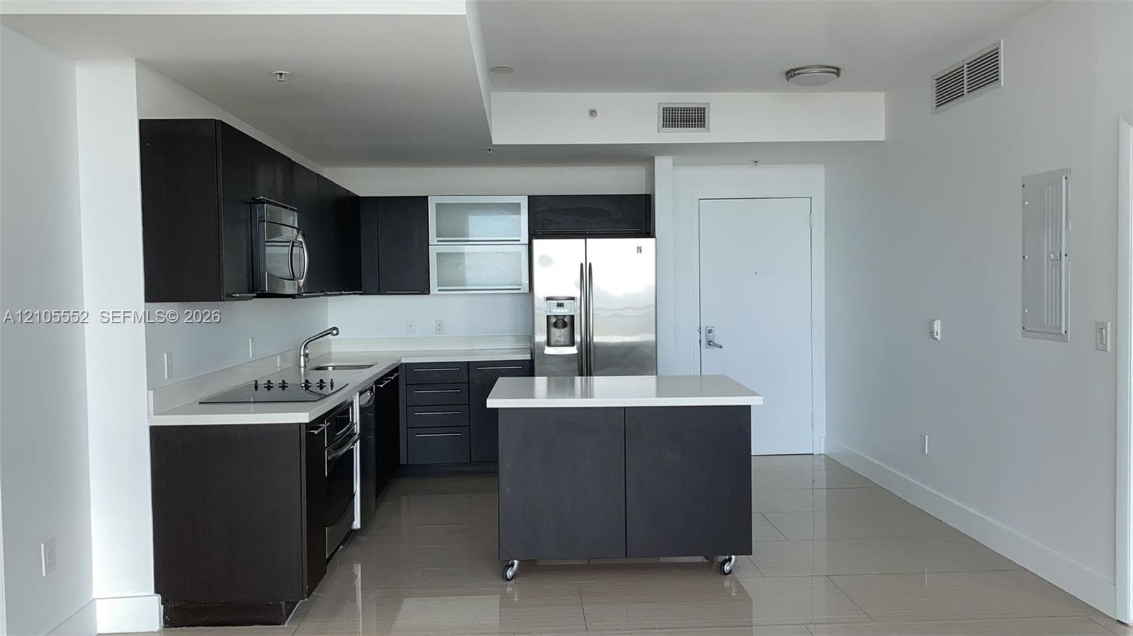 Modern kitchen featuring dark cabinetry, stainless steel appliances, a center island with casters, and light-colored countertops