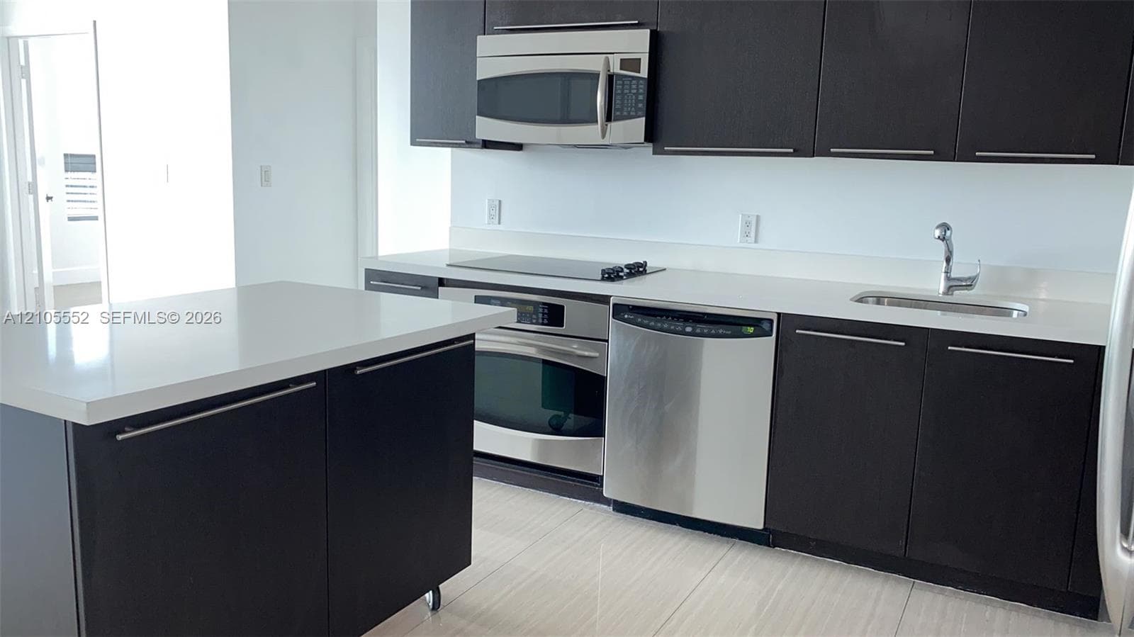 Modern kitchen featuring dark wood-finish cabinetry, stainless steel appliances, light-toned countertops, and an integrated kitchen island