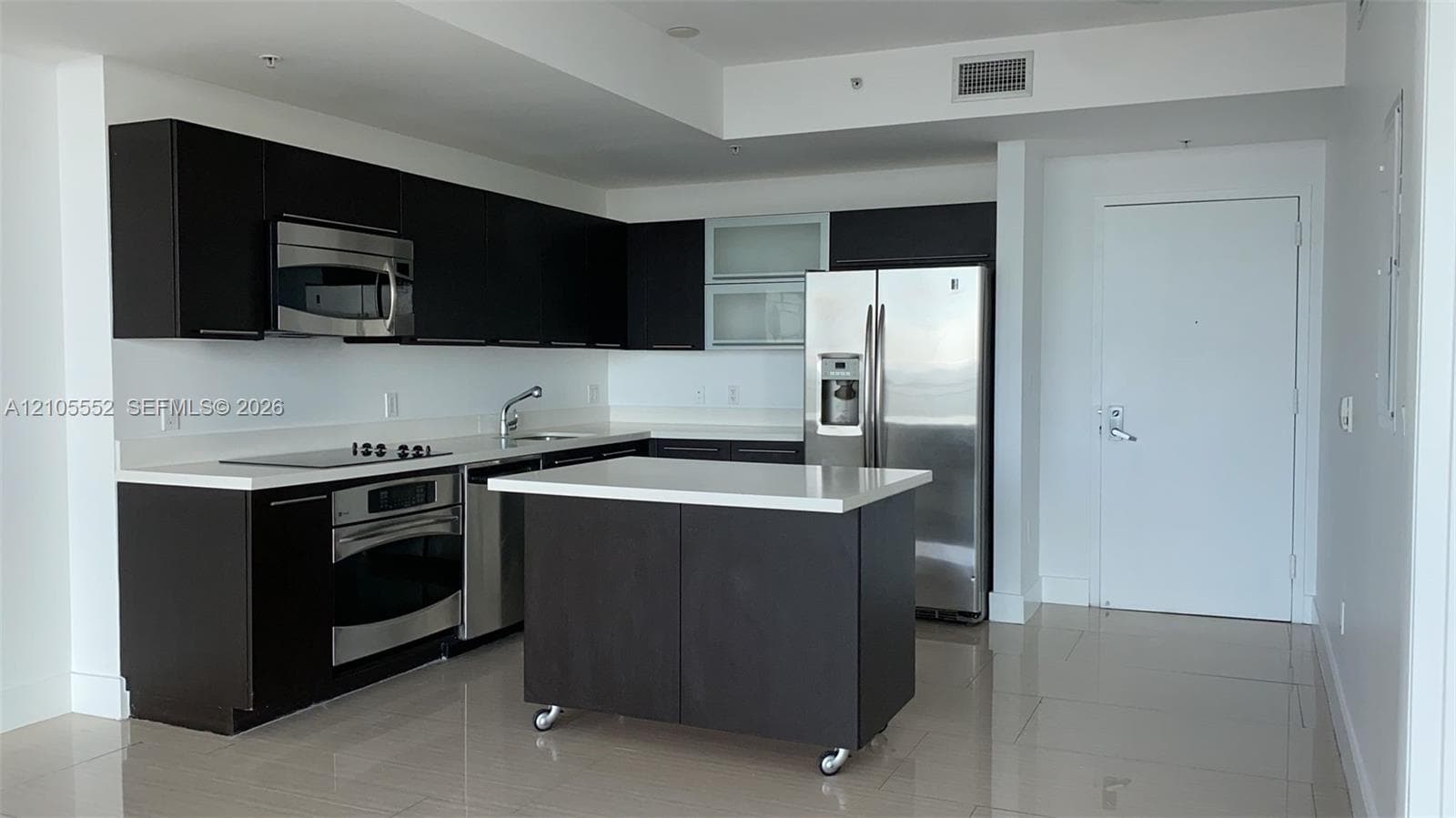 Modern kitchen featuring dark wood-finish cabinetry, stainless steel appliances, a center island, light-toned countertops, and tiled flooring