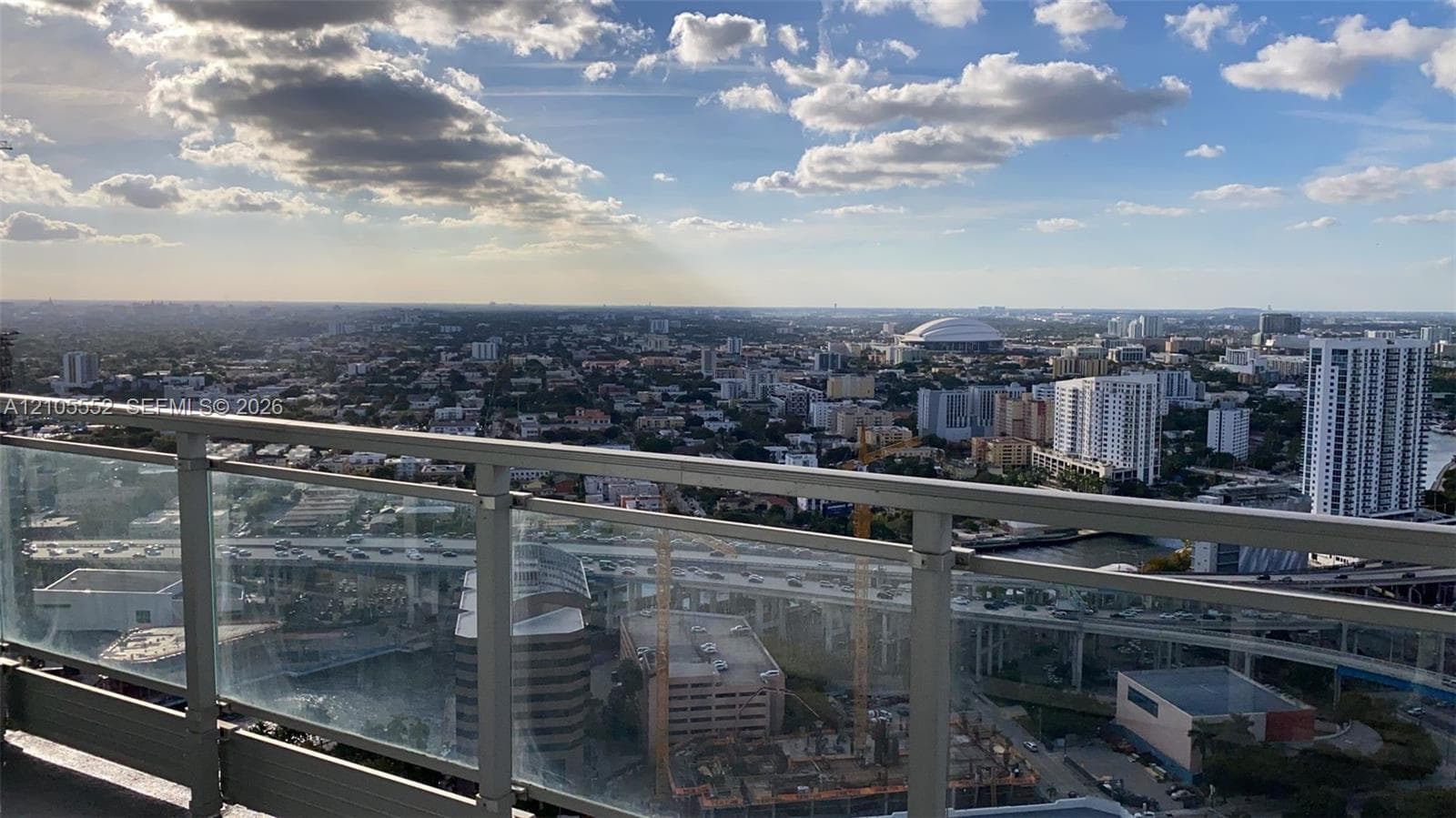 Balcony with glass panel railing and aluminum frame, overlooking an urban landscape with multiple high-rise buildings and infrastructure