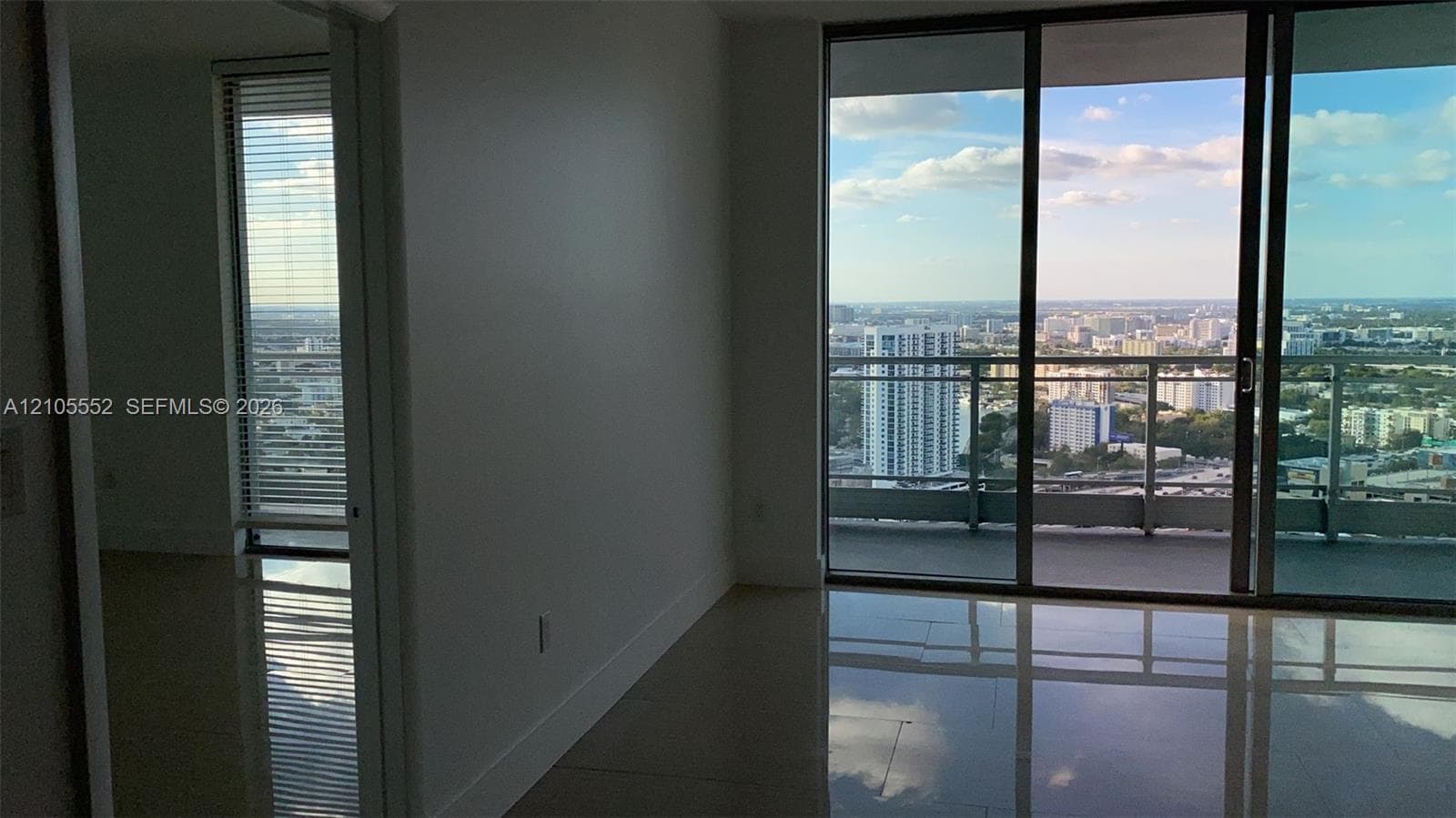 Expansive sliding glass doors, balcony access, tile flooring, and a floor-to-ceiling window