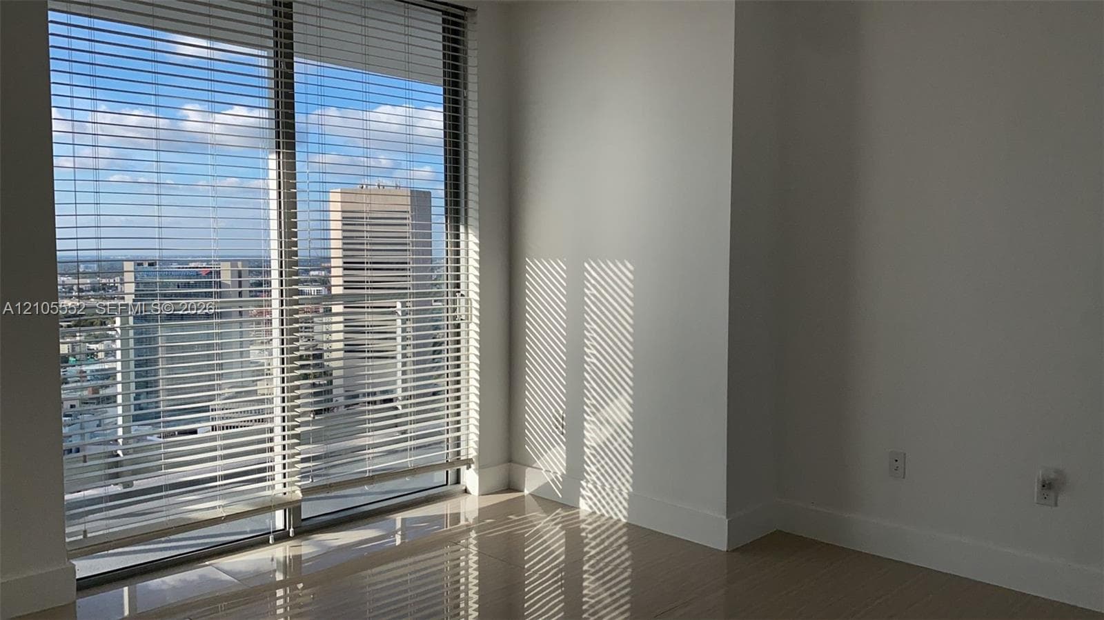 Large window with horizontal blinds, showcasing an expansive cityscape, high-gloss flooring, and clean white walls