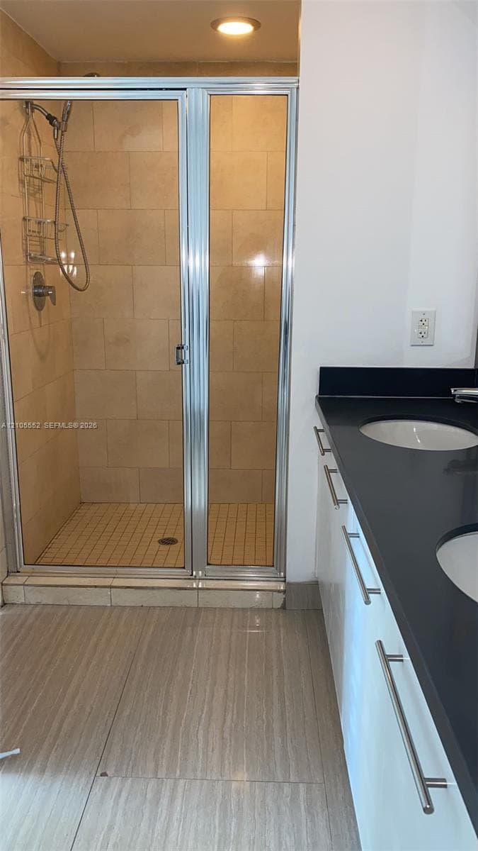 Glass-enclosed shower with subway tile surround, dual basin vanity with dark countertop, and wood-finish flooring
