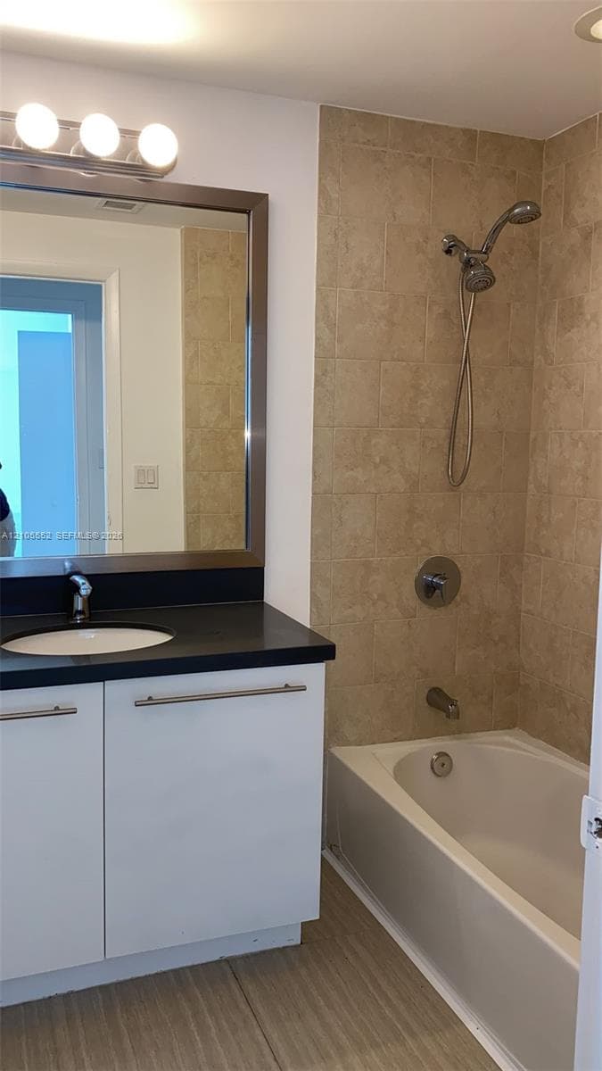 Bathroom featuring a vanity with a dark countertop, white cabinetry with silver-tone hardware, a framed mirror, and a shower-over-tub combination with tiled walls