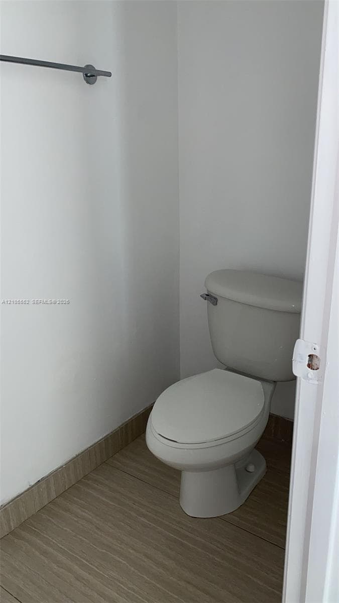 Contemporary toilet with a chrome towel bar and wood-finish tile flooring