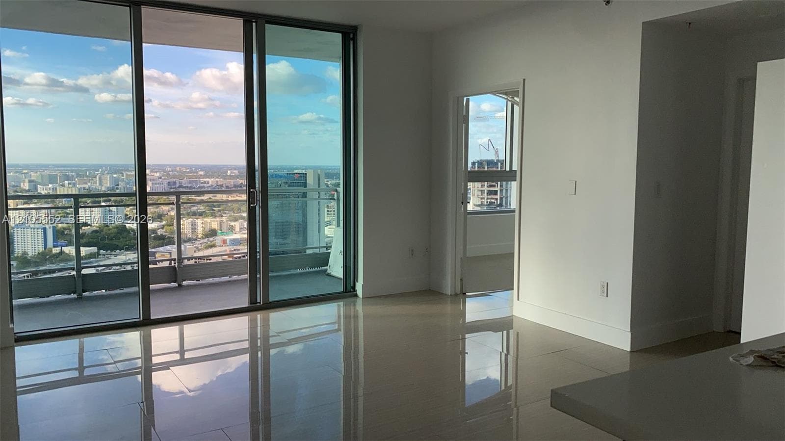 Expansive sliding glass doors opening to a balcony with glass railings, providing elevated city views