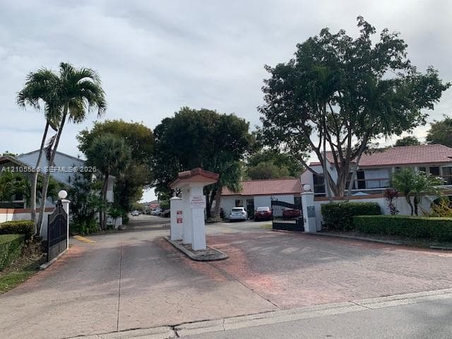 Gated entry featuring a paved driveway, mature trees, and established landscaping