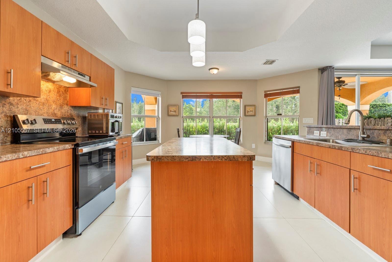 Kitchen featuring wood-finish cabinetry, stainless steel appliances, an island with a stone countertop, and recessed lighting