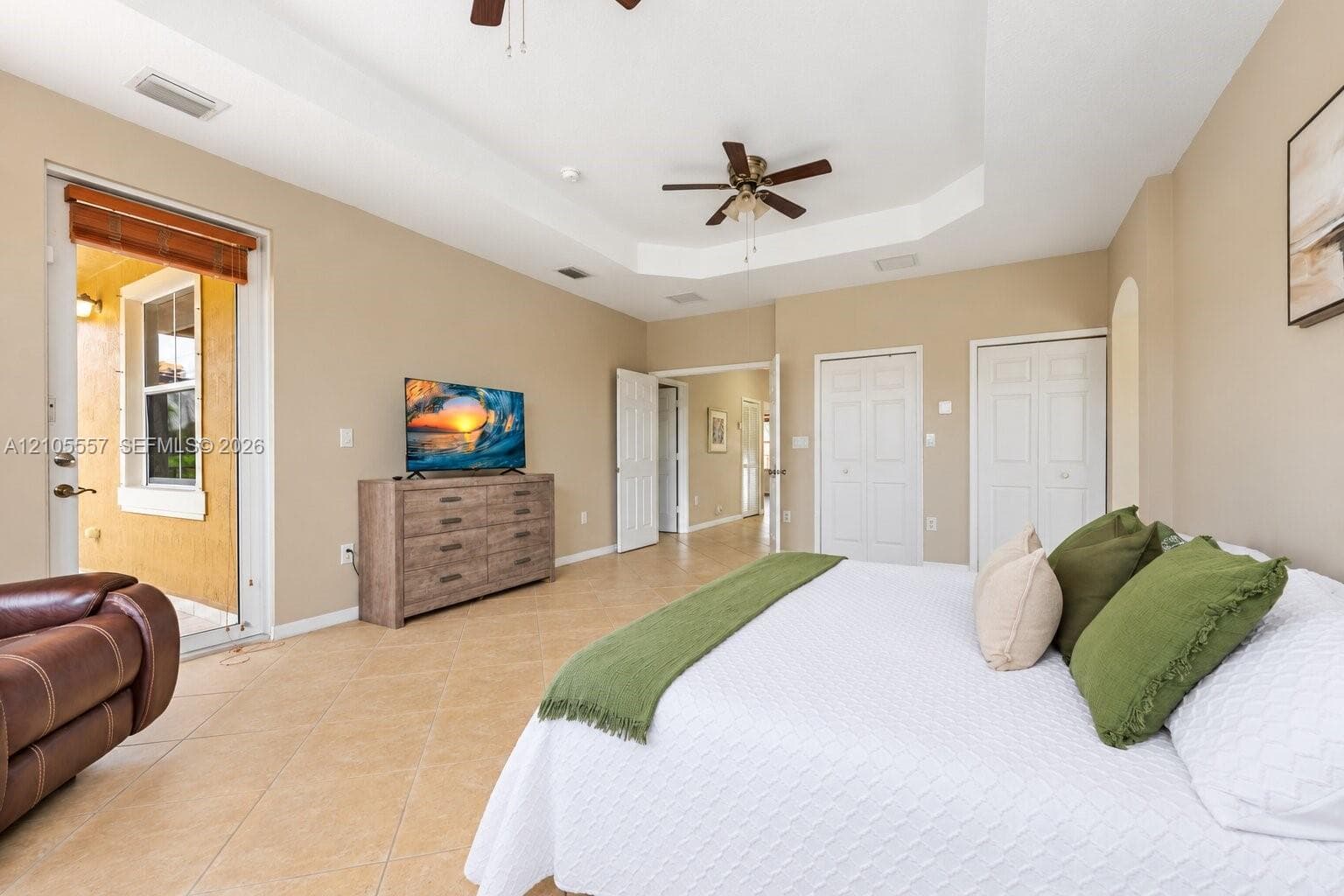 Tray ceiling with a ceiling fan, light tile flooring, and direct access to an exterior patio