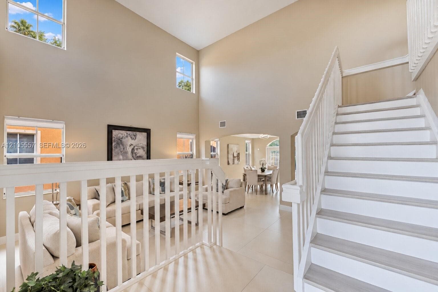 Vaulted ceilings with multiple high windows, white baluster railing, staircase with wood-finish treads, and arched doorway leading to a dining area