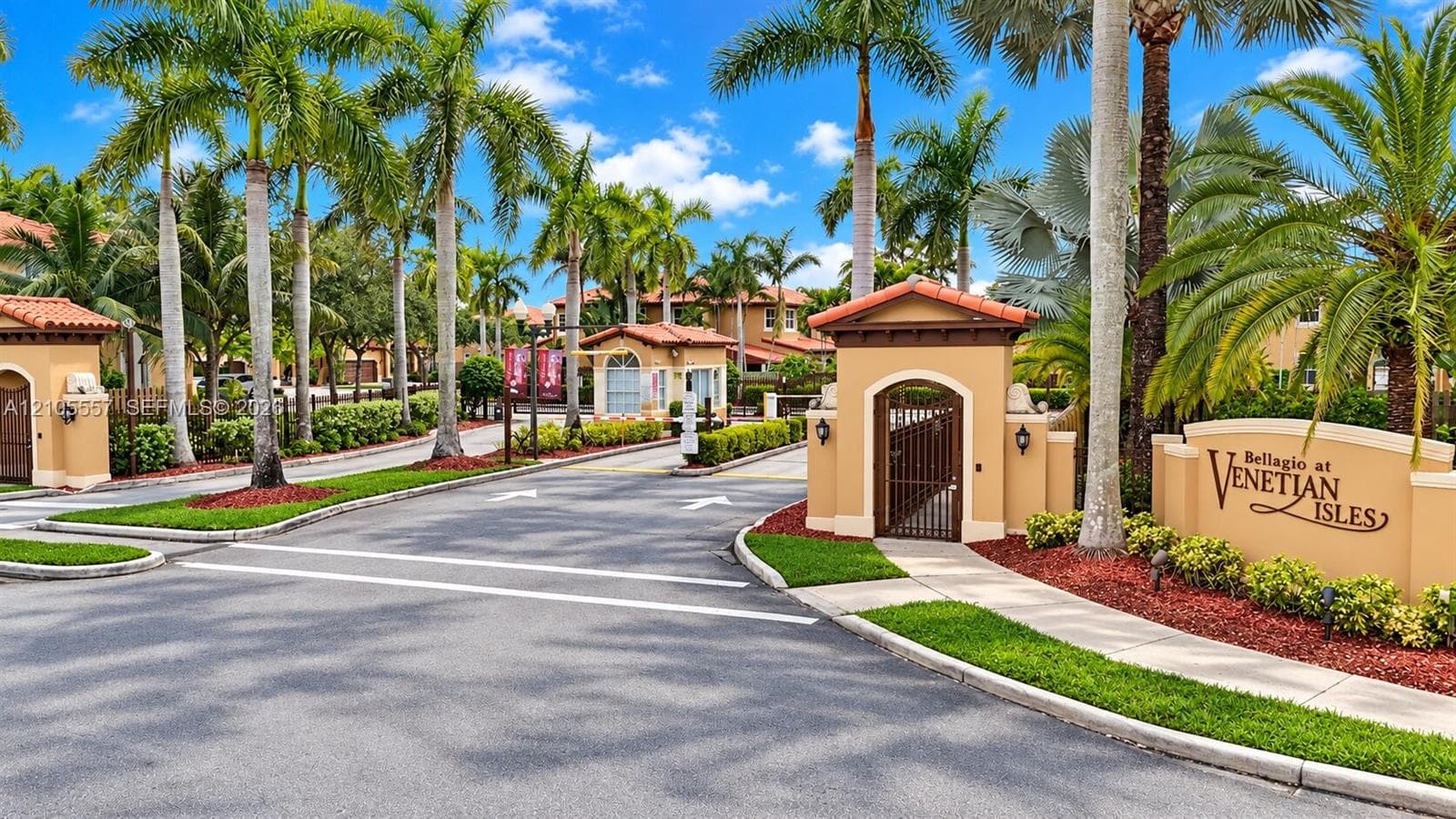 Gated community entrance with a decorative sign, mature palm trees, and manicured landscaping