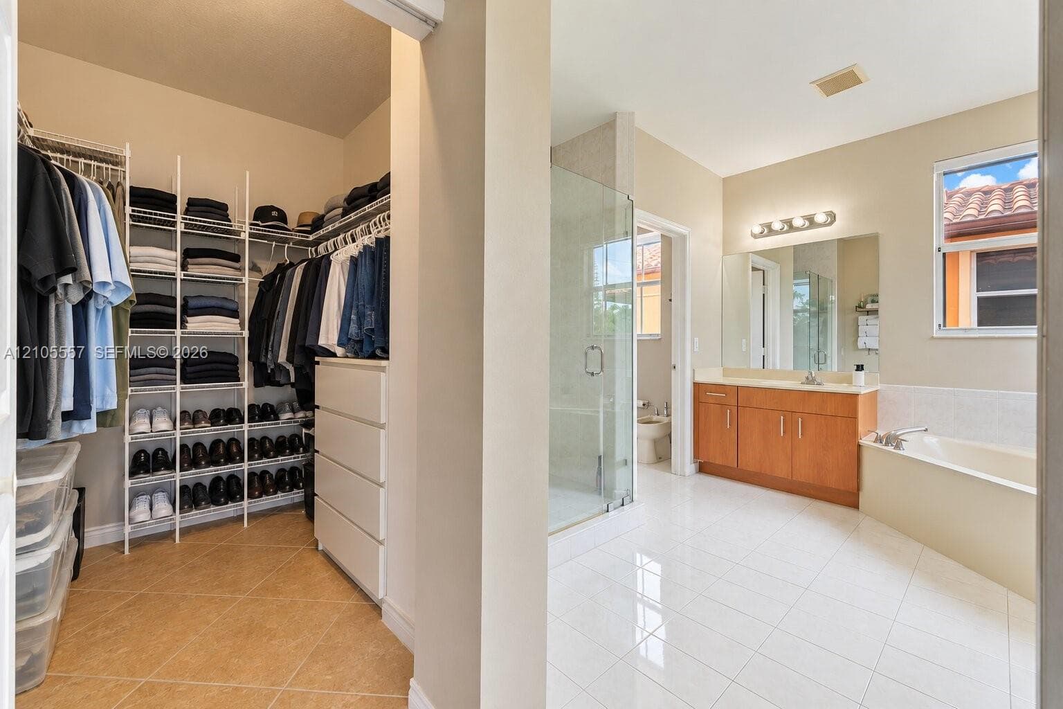 Walk-in closet with built-in shelving, bathroom with a soaking tub, glass-enclosed shower, single vanity with wood-finish cabinetry, and tiled flooring