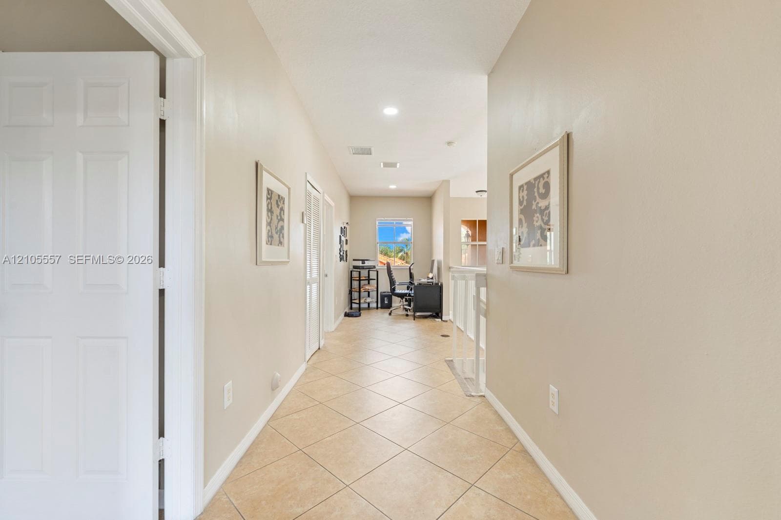Long hallway featuring light-toned tile flooring, recessed lighting, and a window with visible scenery
