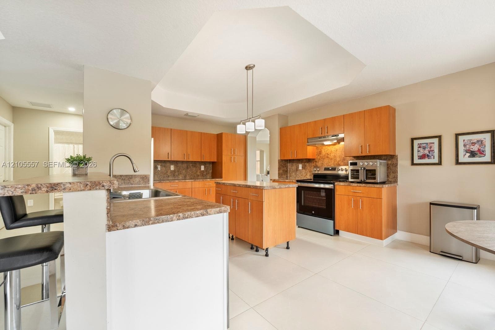 Kitchen featuring a central island, light wood-finish cabinetry, stone countertops, a breakfast bar with built-in sink, and tile flooring