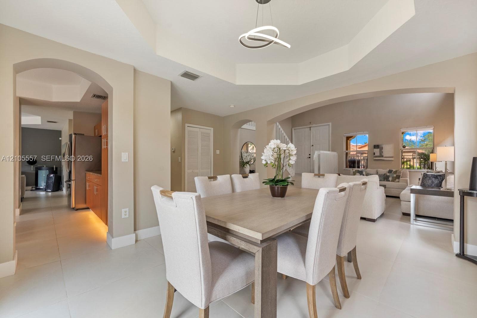 Tray ceiling with a contemporary pendant light fixture, arched doorways, and tile flooring