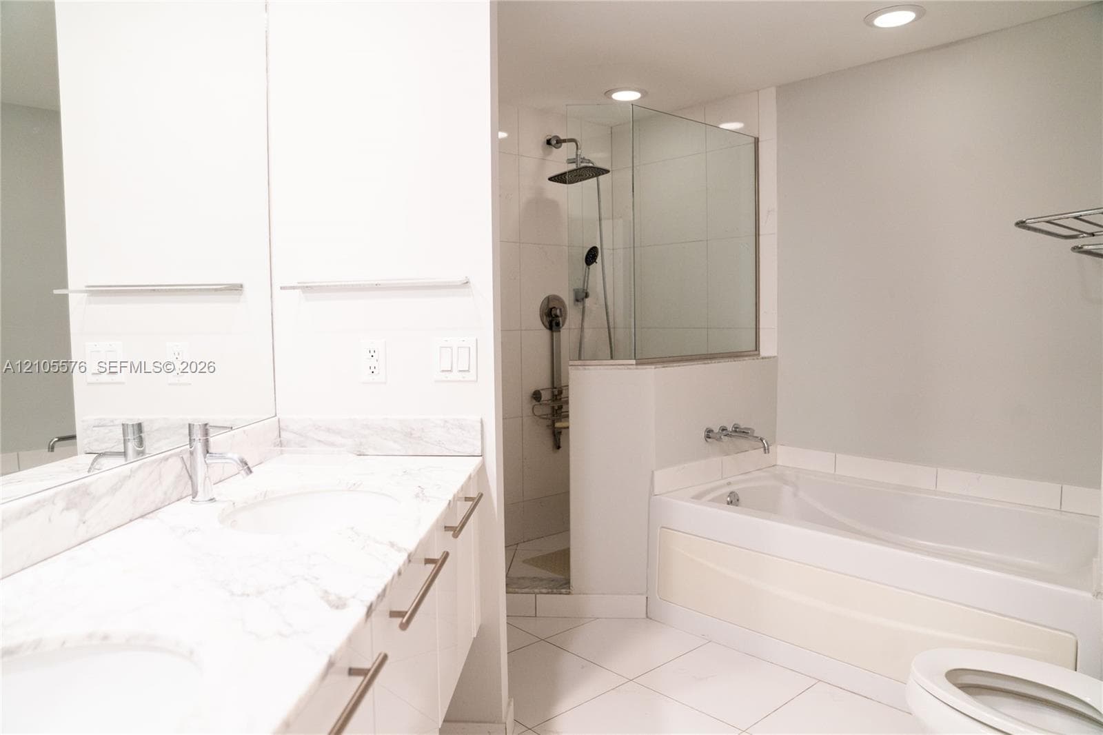 Dual-sink vanity with stone-finish countertop, walk-in shower with glass enclosure and rainfall showerhead, and a deep soaking tub with wall-mounted chrome fixtures