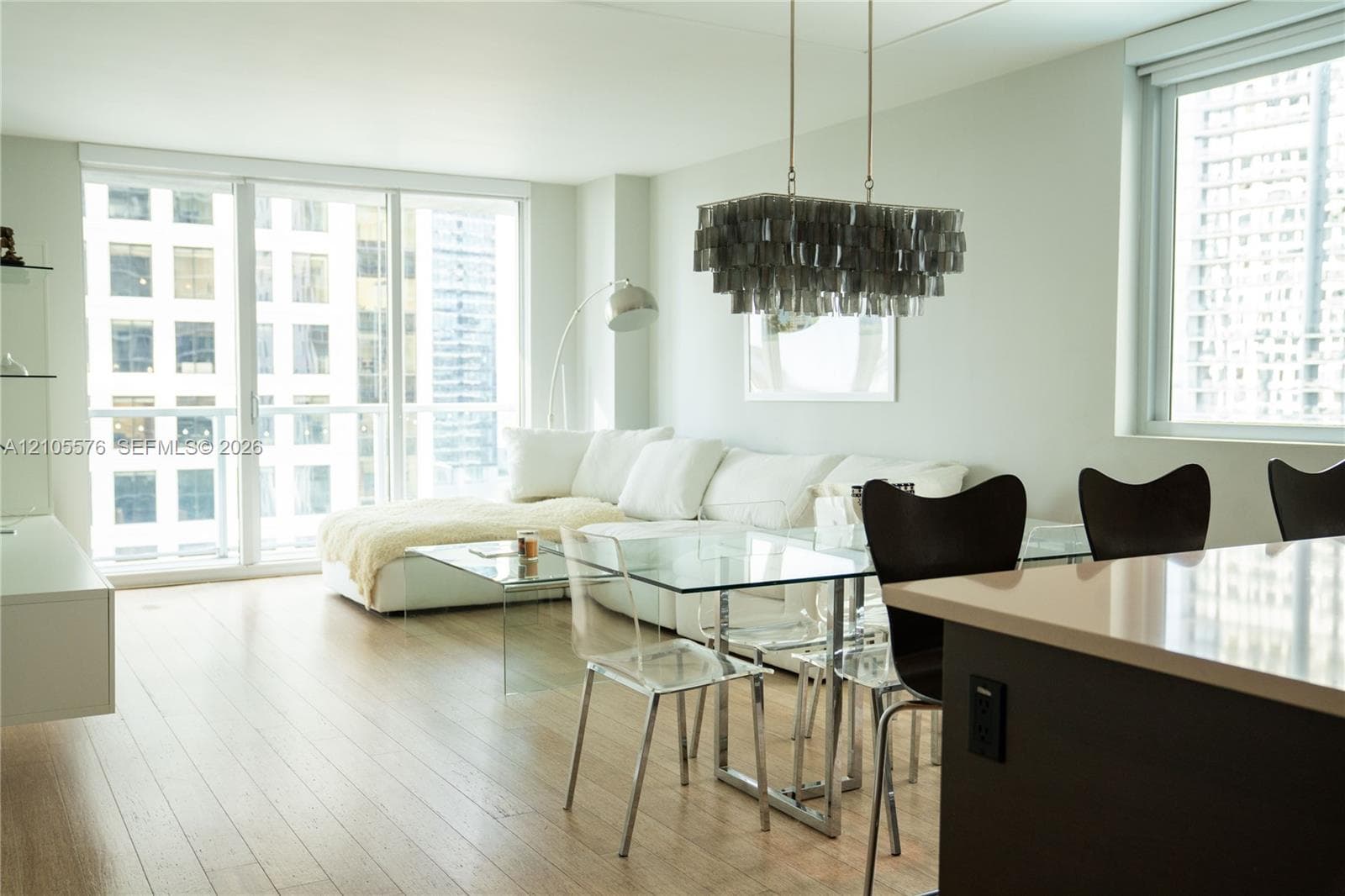 Open-concept living space featuring wood-finish flooring, floor-to-ceiling windows, built-in wall-mounted cabinetry, a central island with a solid surface countertop, and a tiered metallic chandelier
