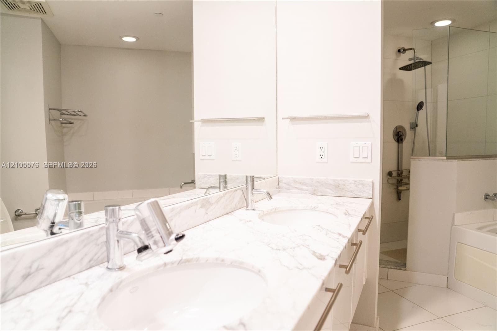 Dual-sink vanity with stone-finish countertops, polished chrome faucets, a full-width wall mirror, and a glass-enclosed shower with a rainfall showerhead