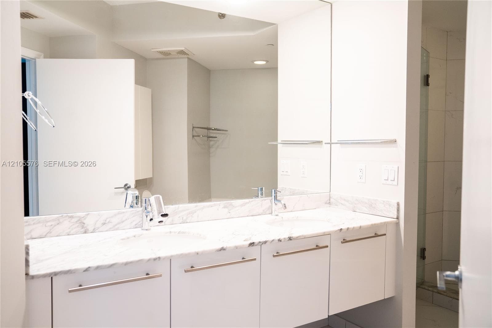 Double-sink vanity featuring stone countertops, white flat-panel cabinetry, modern hardware, and a wall-to-wall mirror