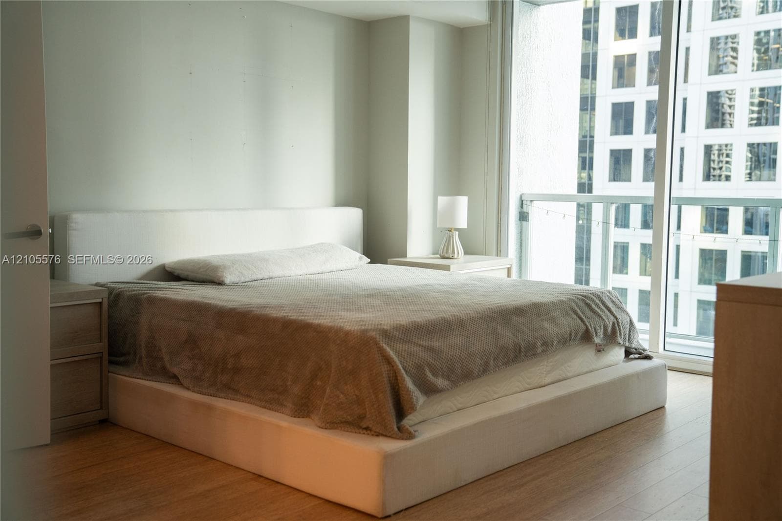 Neutral-toned interior space featuring light wood-finish flooring, floor-to-ceiling windows, and a private balcony with metal railing