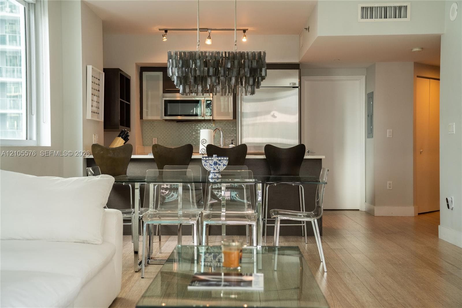 Open-concept kitchen featuring dark-finish cabinetry, stainless steel appliances, and wood-finish flooring, complemented by a distinctive multi-tiered chandelier and a breakfast bar