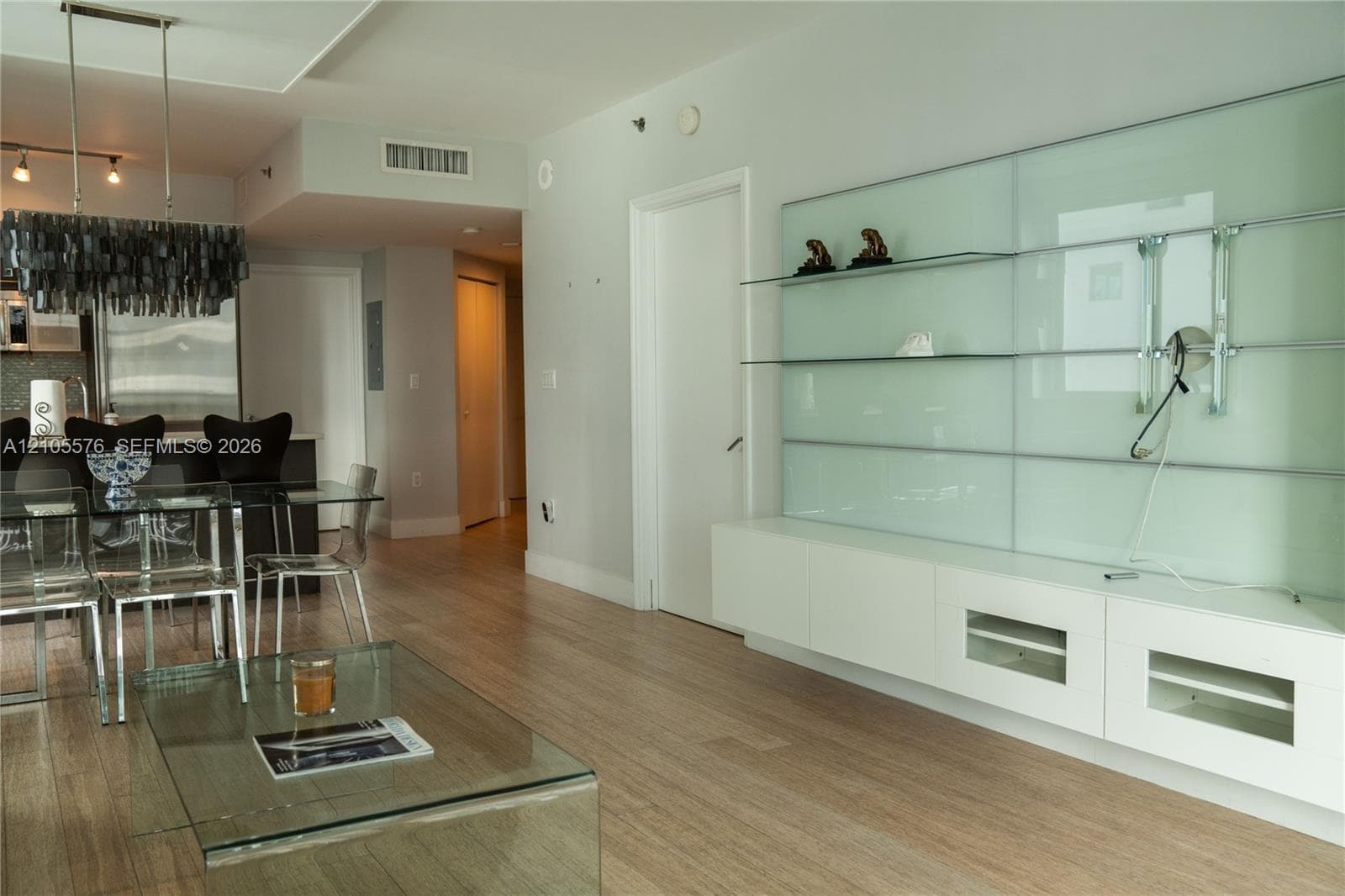 Wood-finish flooring, custom built-in white cabinetry with glass shelving, and a linear pendant light fixture