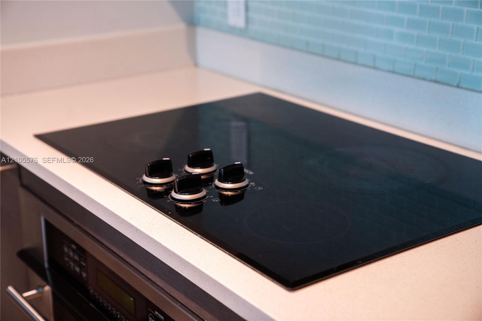 Black glass cooktop set into a white solid-surface countertop with a light blue glass subway tile backsplash