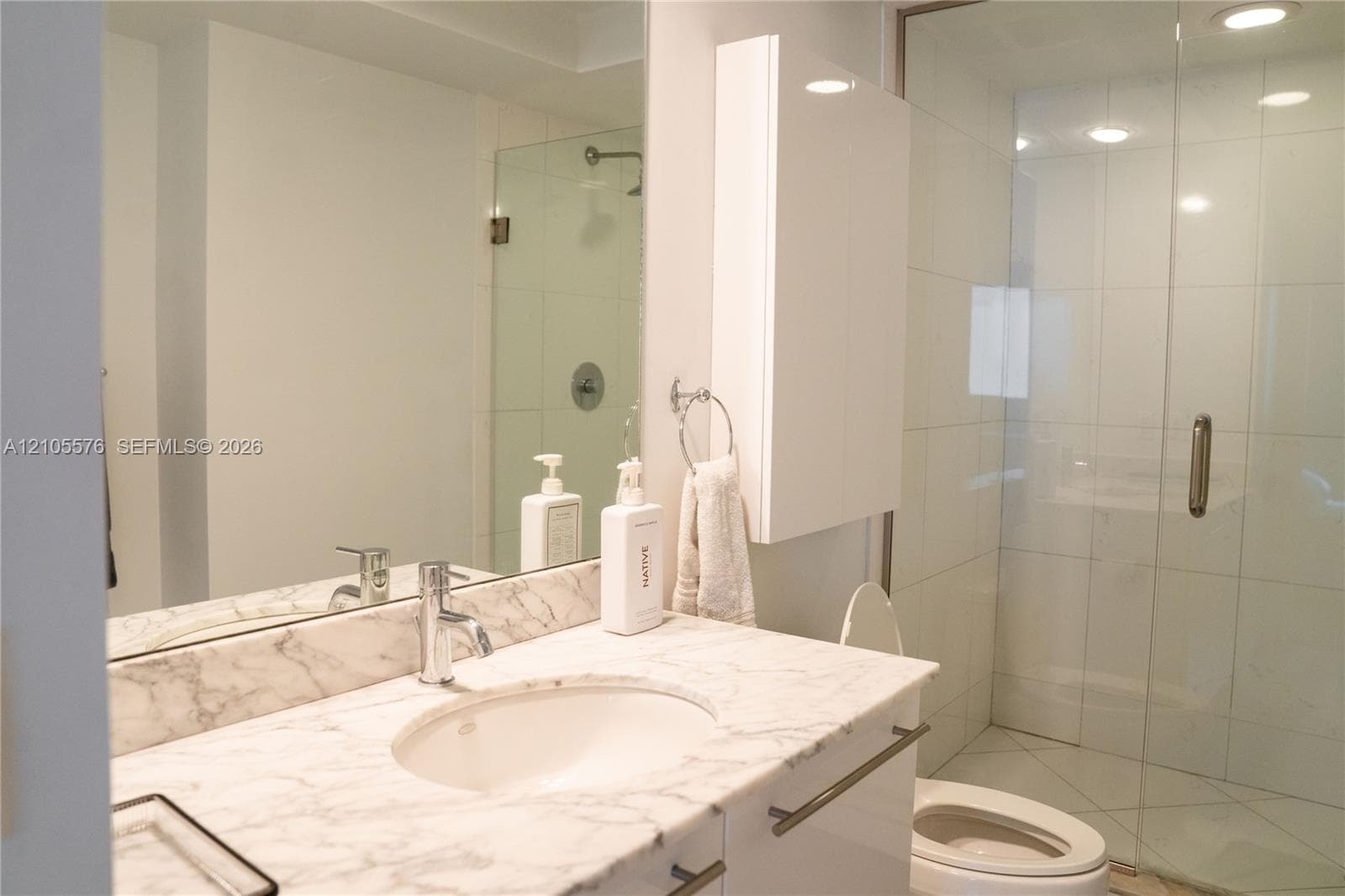 Bathroom featuring a stone-surface vanity with an integrated basin, wall-mounted medicine cabinet, full-width mirror, and a glass-enclosed walk-in shower with tile surround