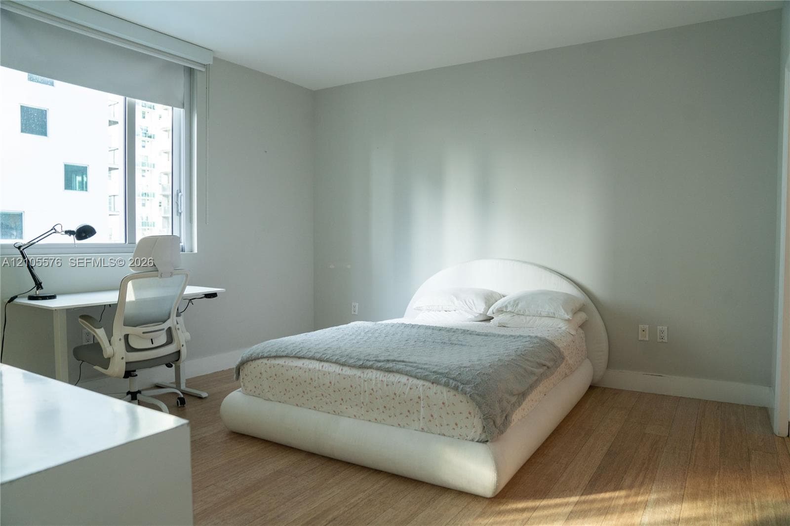 Light-filled room featuring wood-finish flooring, neutral wall tones, and a large window with an integrated roller shade