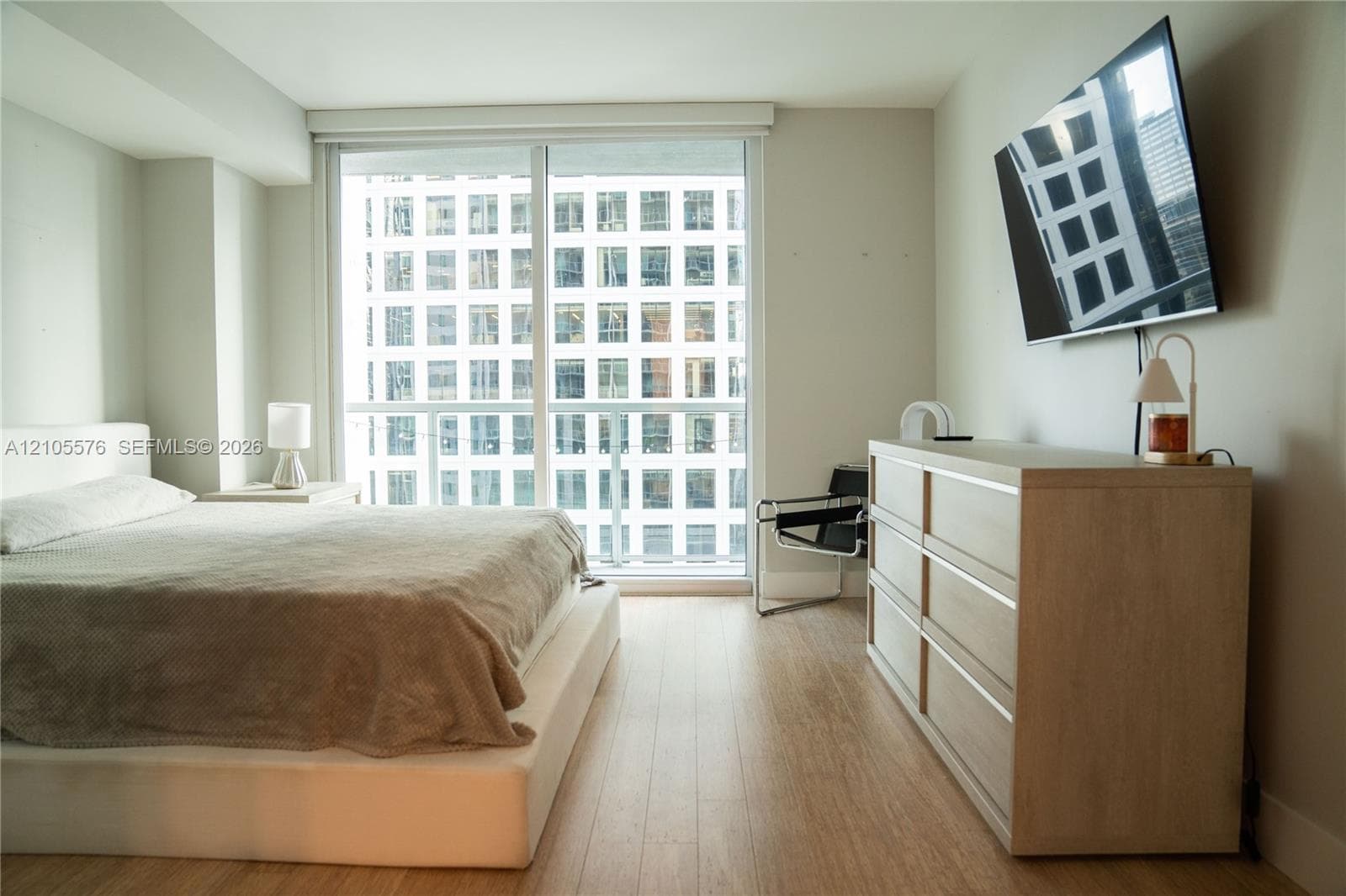 Floor-to-ceiling glass sliding door with access to a private balcony, wood-finish flooring, and neutral wall tones