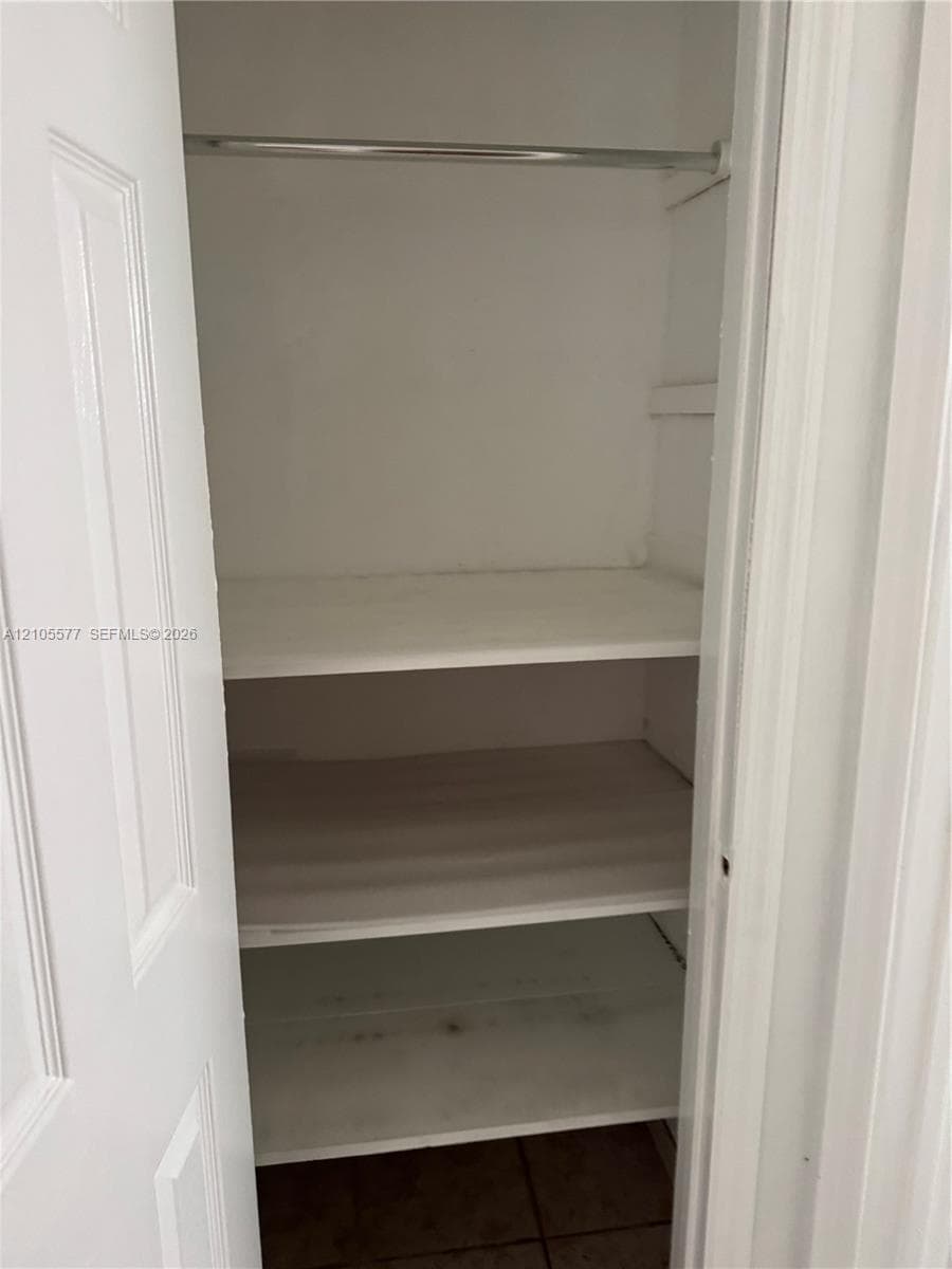 Storage closet featuring white-painted wood shelving and a metal garment rod