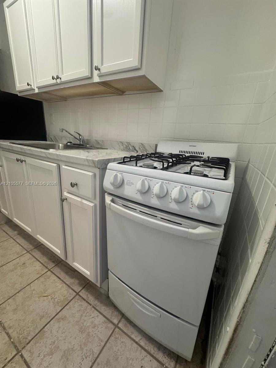 White upper and lower cabinetry, a stainless steel sink, a white gas range, and a tiled backsplash