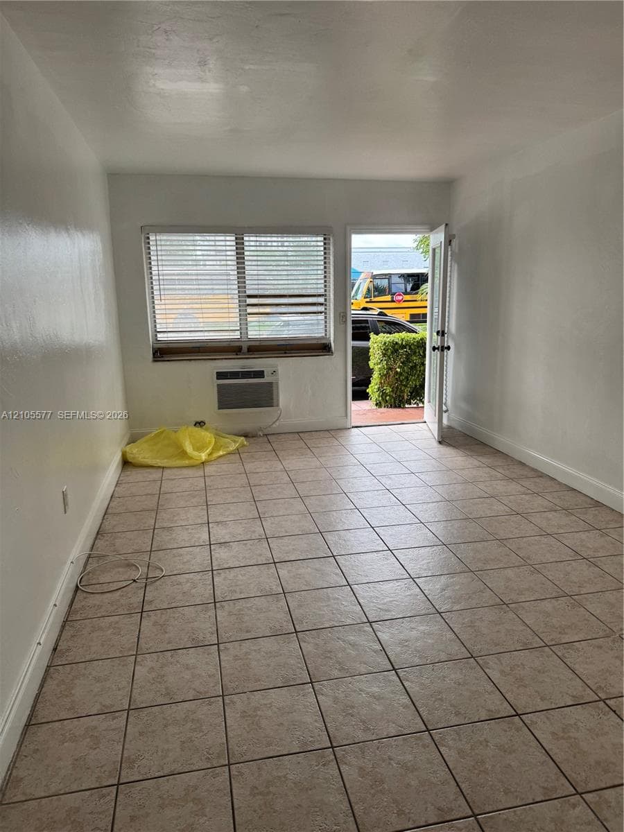 Interior space featuring ceramic tile flooring, neutral wall finishes, a window with horizontal blinds, and a built-in wall air conditioning unit