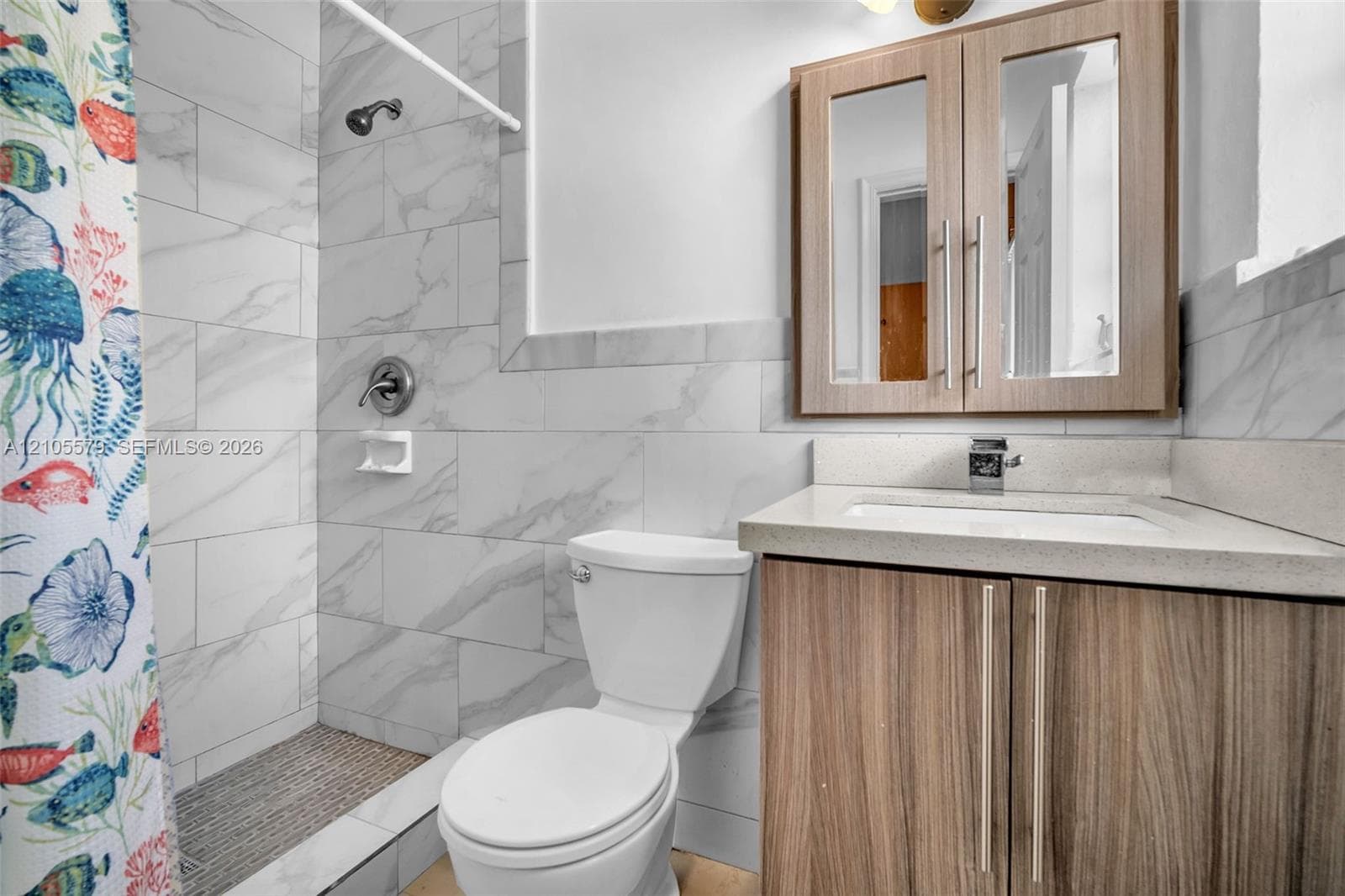 Bathroom featuring a vanity with a light-toned countertop, wood-finish cabinetry, a mirrored medicine cabinet, and a walk-in shower with large-format stone-patterned wall tile