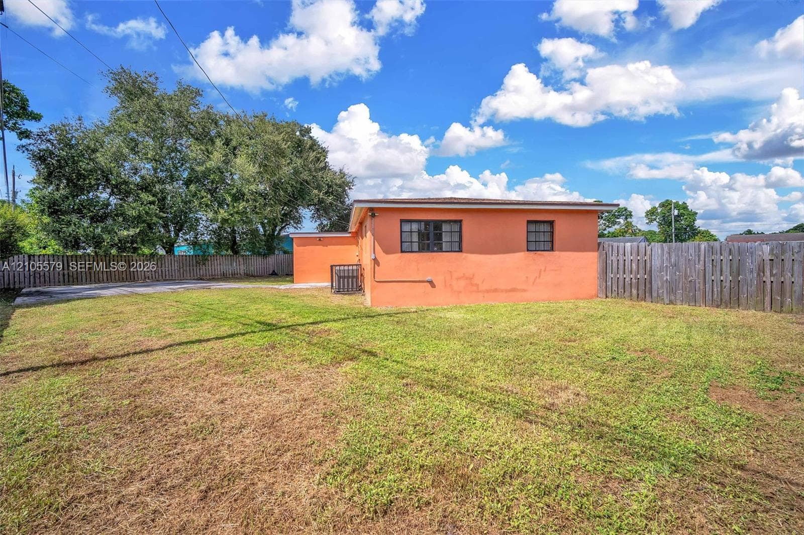 Exterior of the residence featuring a concrete masonry unit wall finish, rectangular grid windows, and an expansive rear yard enclosed by wooden perimeter fencing