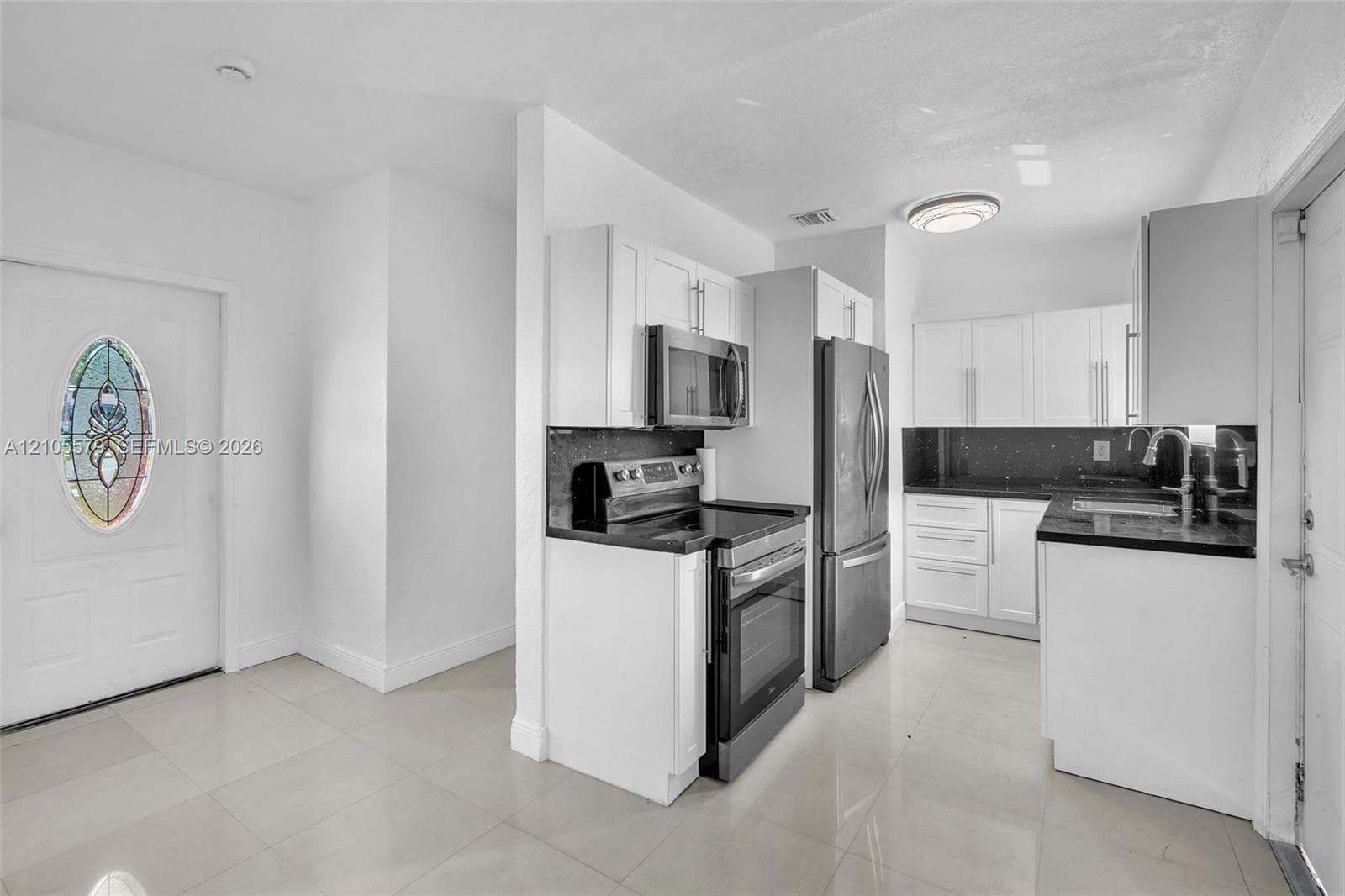 Kitchen featuring white shaker-style cabinetry, stainless steel appliances, dark countertops, tile flooring, and a door with a decorative oval glass insert