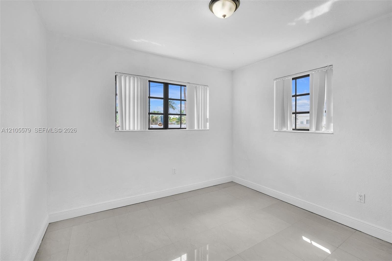 Interior space featuring large-format ceramic tile flooring, neutral wall finishes, two multi-pane windows with dark frames, and a central ceiling-mounted dome fixture
